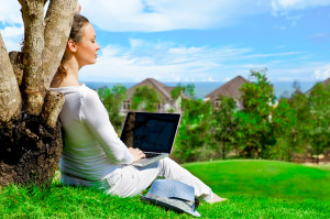 Young woman sitting under tree with laptop and dreaming. Idyllic outdoor scenery